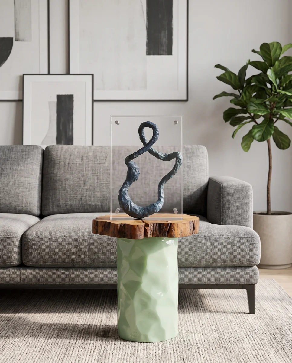 An AI-generated lifestyle photo: a dark abstract sculpture in a clear acrylic mount, standing on a live-edge wood and pale-green ceramic side table beside a grey sofa